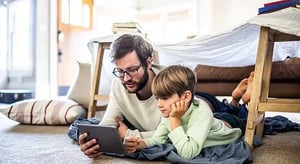 Un père et son fils allongés ensemble sur le sol et regardant une tablette