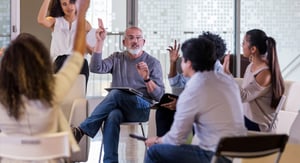 Un grupo diverso de personas en una sala de reuniones informal participan activamente en una discusión con una persona que dirige la conversación.