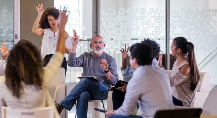 Diverse group of people in a casual meeting room actively engaging in a discussion with a person leading the conversation.