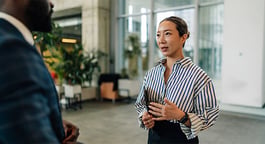 A woman gesturing while speaking to a coworker in a bright, contemporary workplace