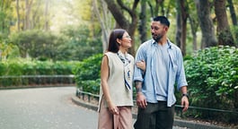 A smiling couple walking arm-in-arm through a lush, green park
