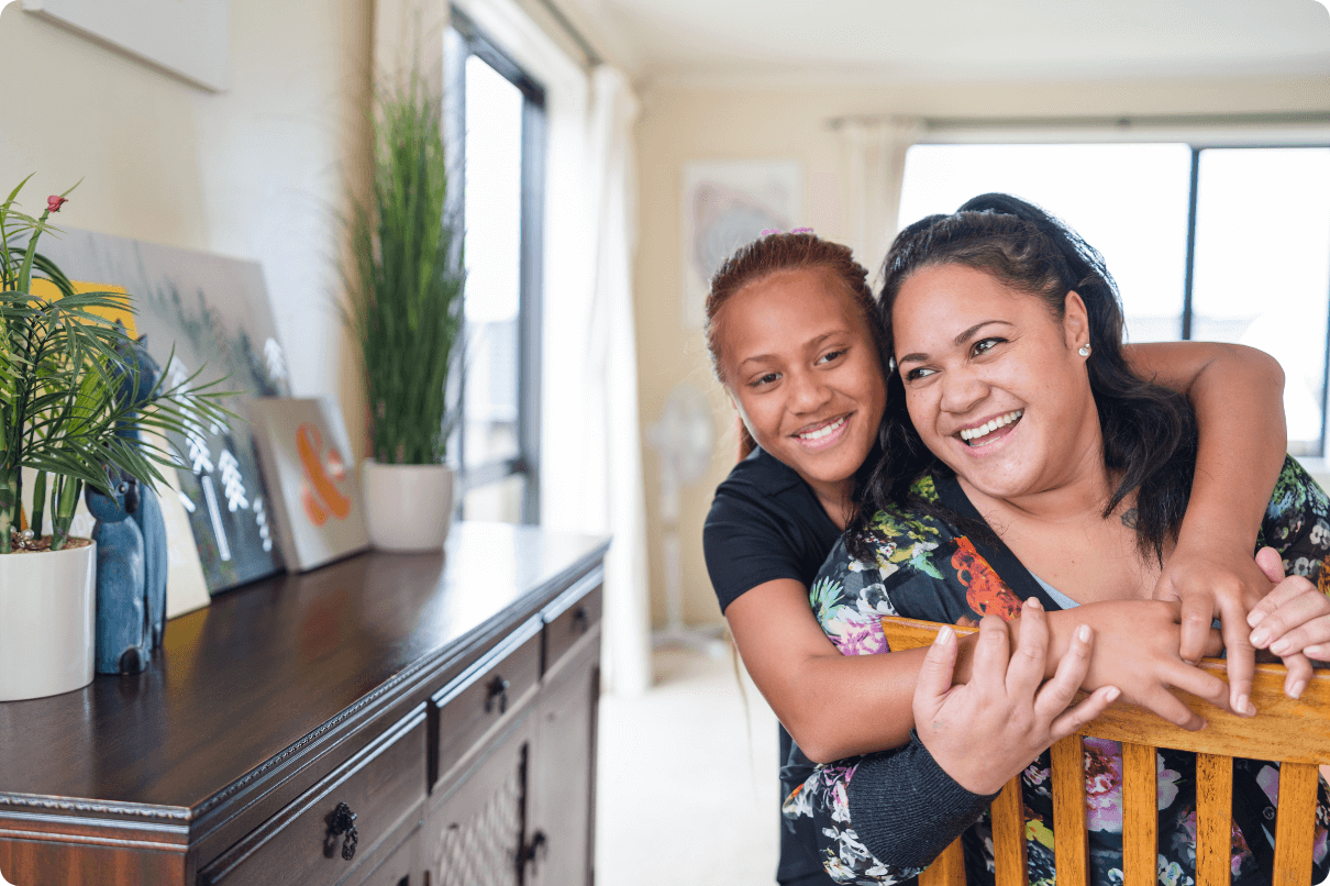 A mother and daughter are happy and smiling as they embrace around the dining table