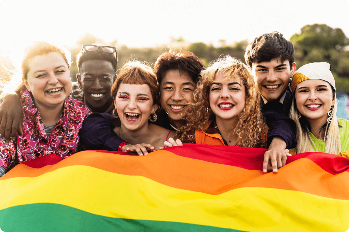 Un grupo de jóvenes multiculturales sonrientes se paran frente a una colorida bandera.