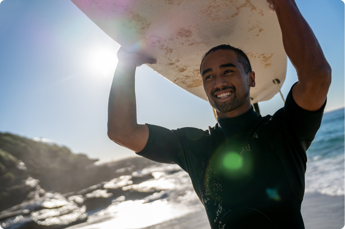 Man smiling and holding a surfboard as he exits the ocean after a surf