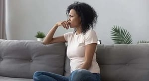 a-woman-sitting-on-a-couch-resting-her-head-on-her-hand,-looking-into-the-distance