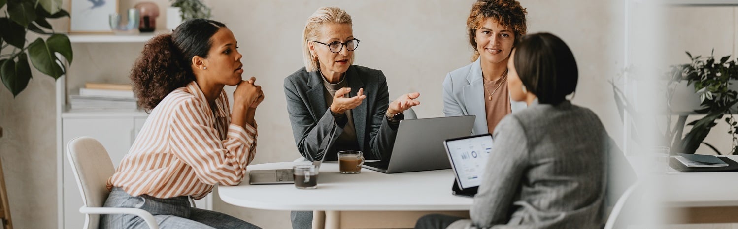 Four women sitting at a boardroom table talking
