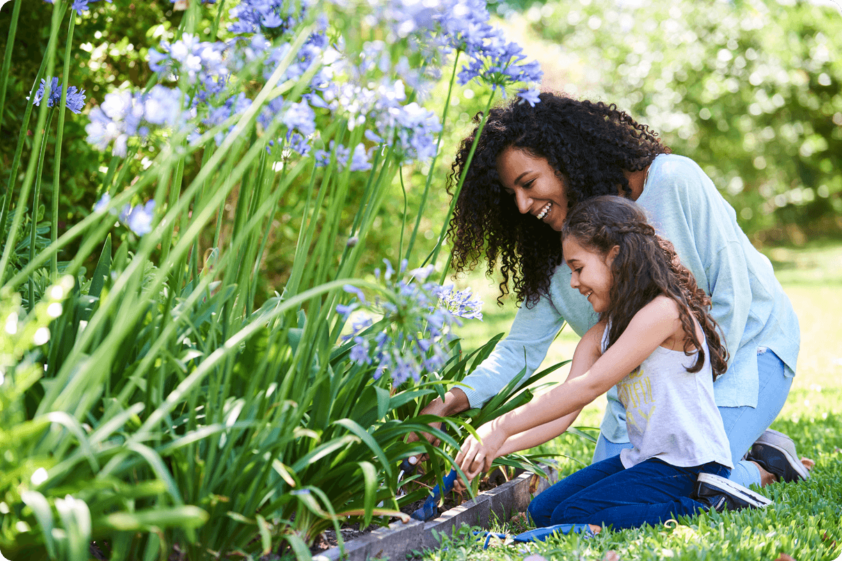 A smiling woman and young girl dig in an outdoor flower garden. 