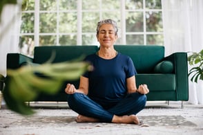 Une femme assise par terre, les jambes croisées et les yeux fermés.