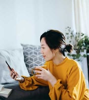 Femme buvant un café regarde son téléphone dans un salon