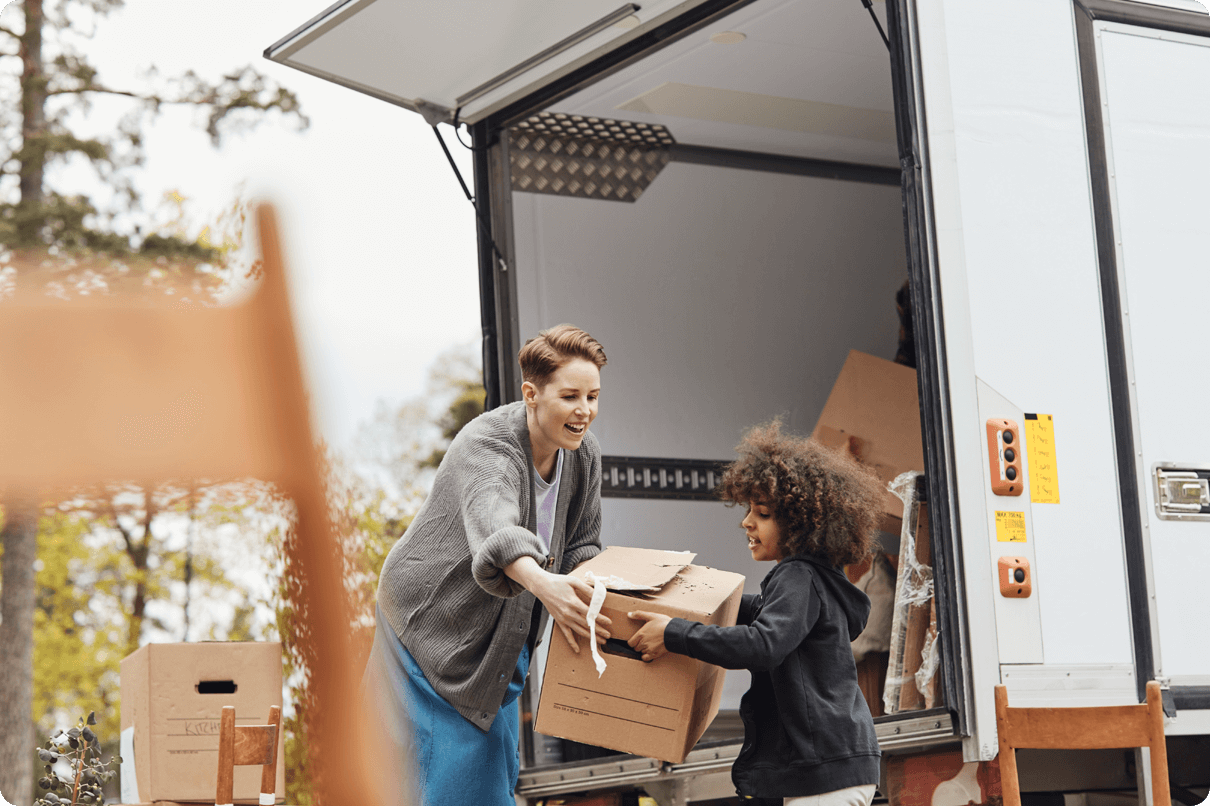 A woman in the back of a moving truck gets help with a box from a young man. 