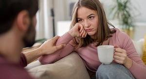 A woman sitting on a couch holding a cup of coffee, looking concerned