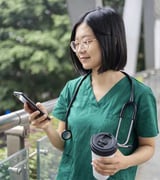 Women with glasses wearing medical clothing looking at her phone