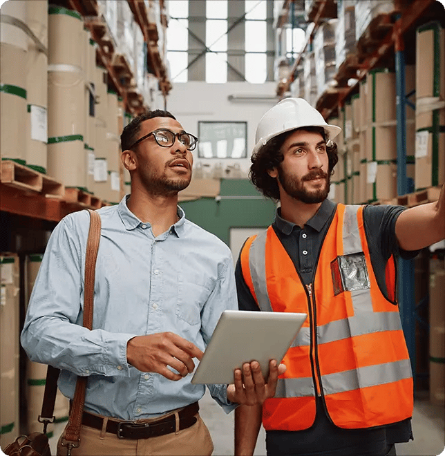 Two people, one wearing a hard hat and safety gear and the other in a formal outfit, are pointing at something
