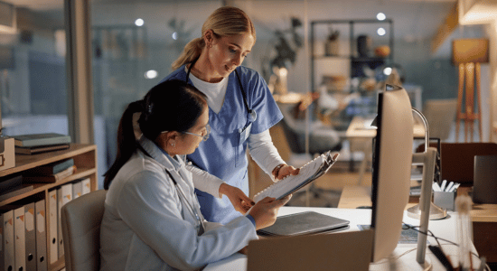 Two healthcare workers review information together at a workstation during a night shift.