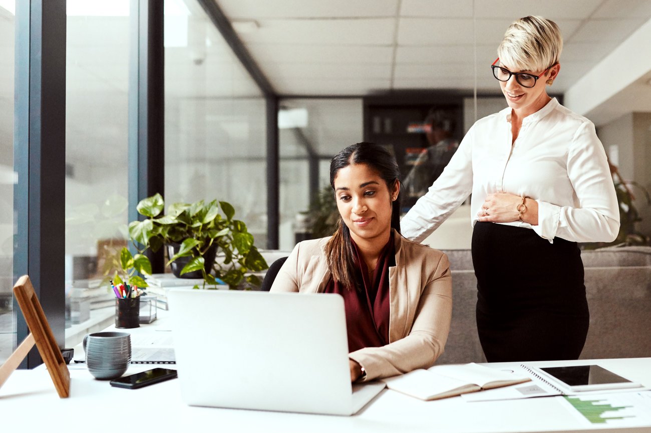 Two women collaborate in an office, focused on a laptop, engaged in a productive discussion.