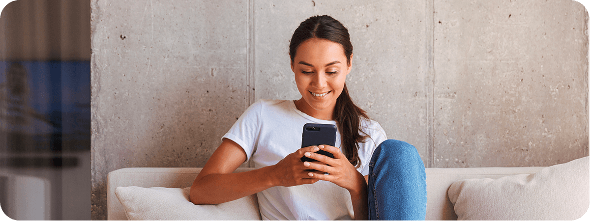 A young woman looks at her smartphone while sitting on her couch