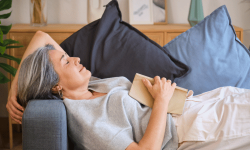 Senior woman falling asleep while reading a book on the sofa