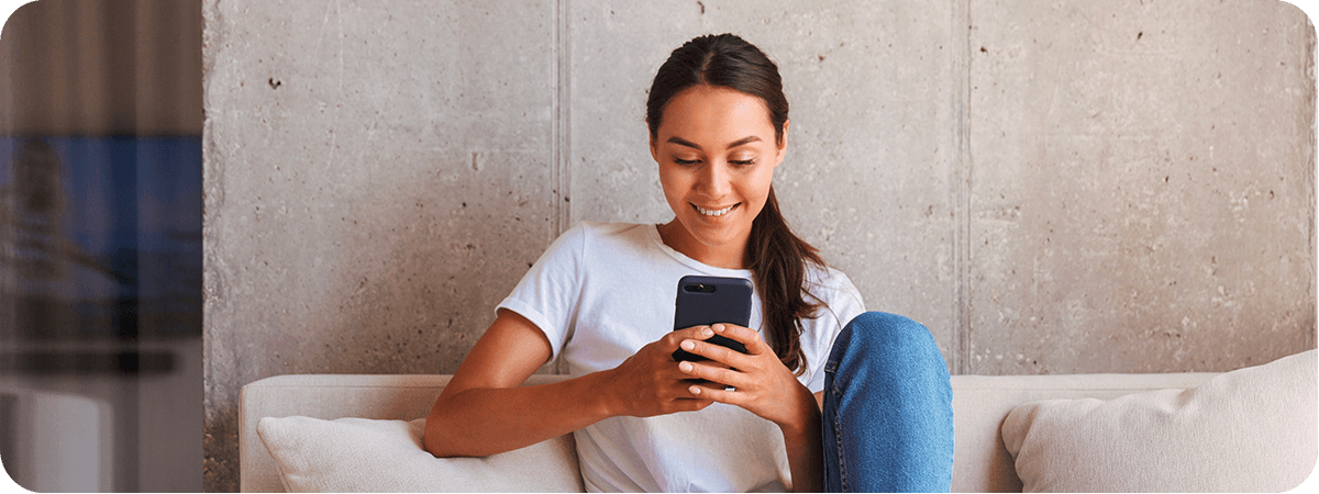 Une jeune femme regarde son smartphone assise sur son canapé