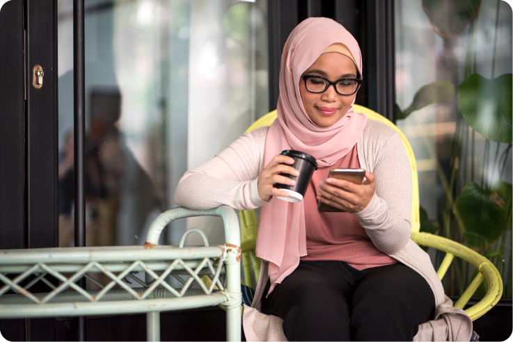 A woman sitting outside holding a coffee and looking at her phone